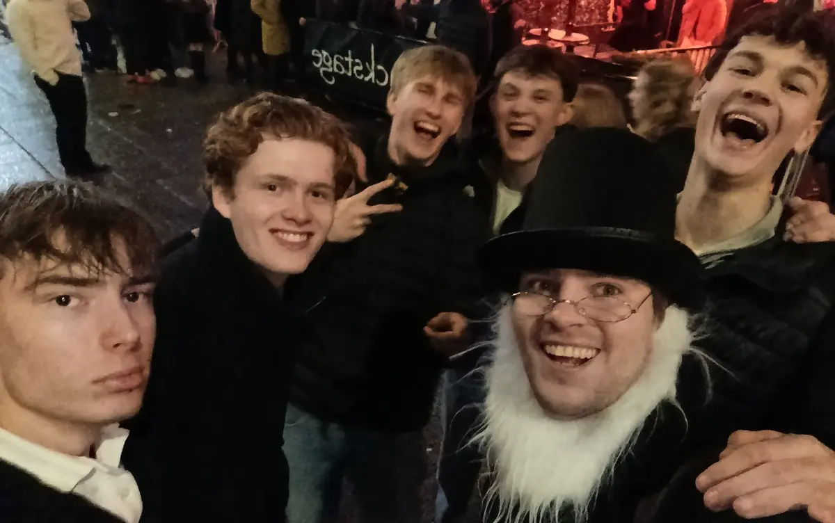 Magnus dressed as Ibsen smiling with a group of young people